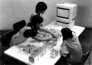 Children collaboratively programming with AlgoBlock, arranging physical blocks on a table while a computer displays a submarine simulation.