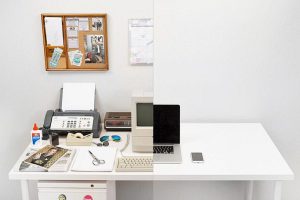 A split view between an office of the ’80s and today’s desktop with only a laptop and a phone