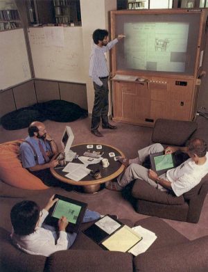 Xerox PARC researchers collaborating around a live digital board, illustrating early ubiquitous computing experiments with networked displays and active badges